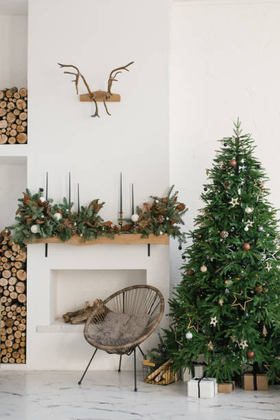 istock Stylish Scandinavian minimalistic Christmas interior with fireplace and Christmas tree. Cozy house. Modern interior of a country house with firewood 1826962432