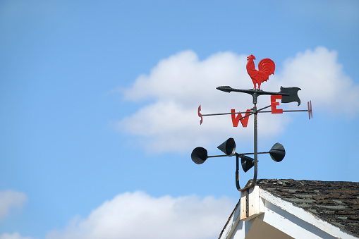 Traditional weather vane with cockrell motif and anemometer with blue sky and cloud background for copy.