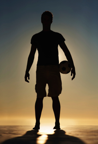 Silhouette image of a confident man holding a soccer ball against sunset