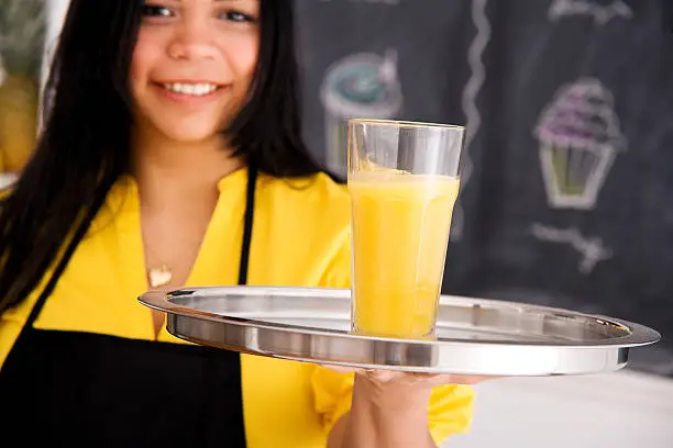 Photo of Cafe Employee Standing & Holding Orange Juice on a Tray