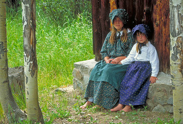 Pioneer Girls "Young girls in early American, pioneer-type clothing in authentic rustic setting." bonnet hat stock pictures, royalty-free photos & images
