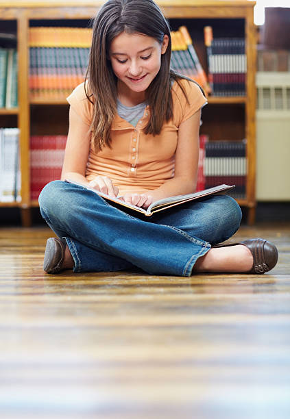istock Smiling school girl reading a book while at the library 182699043