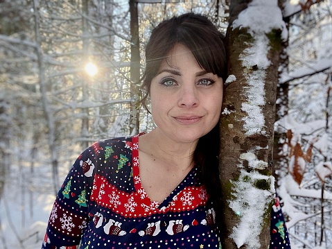 Beautiful brown haired and blue eyed middle aged active and healthy woman, playing and enjoying the outdoors in a sun and snow covered forest in Northern Wisconsin in December with a Christmas shirt and white snow pants on.