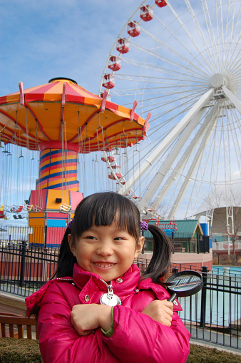 Happy little girl in front of the chain swing ride and ferris wheel