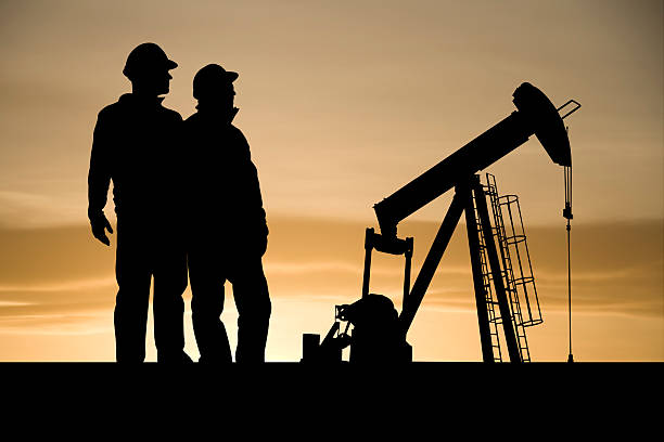 Icons of the Oil Industry Two industry workers stand next to an iconic symbol of the oil and gas industry - an oil pumpjack. oil pump oil industry alberta equipment stock pictures, royalty-free photos & images