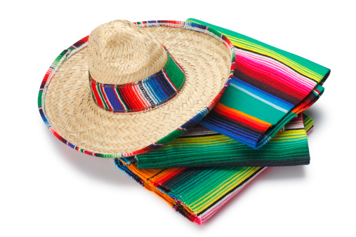 A Mexican sombrero sitting on a stack of Mexican blankets on white background. Clipping path included