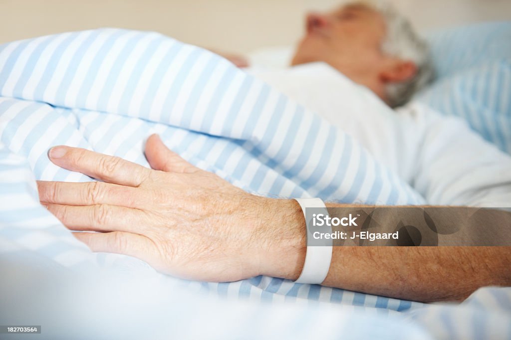 Hombre yacer en la cama de hospital con una banda en mano - Foto de stock de Cama libre de derechos
