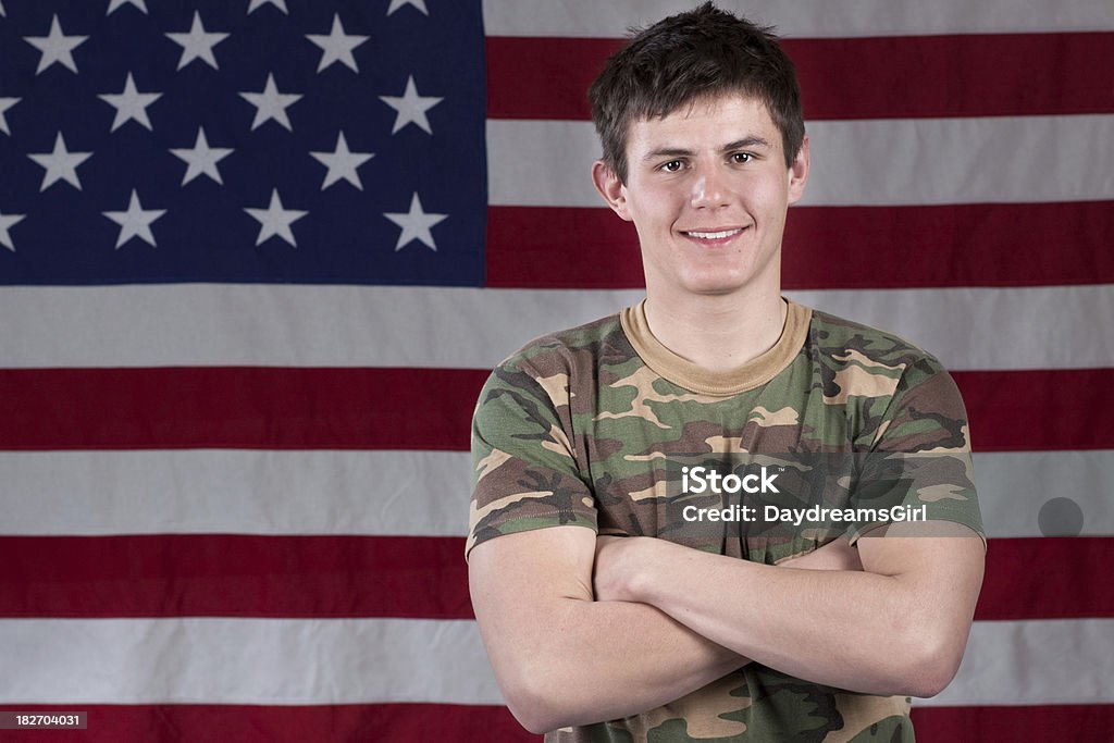 Smiling Patriotic American Happy oung man wearing camouflage shirt and arms crossed with American flag in background. Arms Crossed Stock Photo