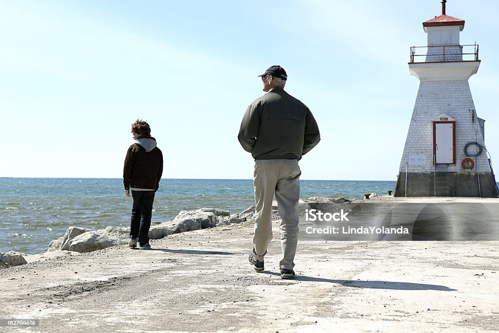 Grand-père et son petit-fils marchant le long de la jetée - Photo de 60-64 ans libre de droits