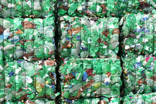Close-up of compressed paper and plastic gathered into bundles and stacked outdoors at waste management facility.