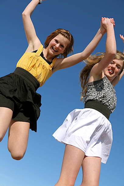 Two beautiful 13 year old girls jump for joy against a bright blue sky. Shot with a Canon 5D Mark II.