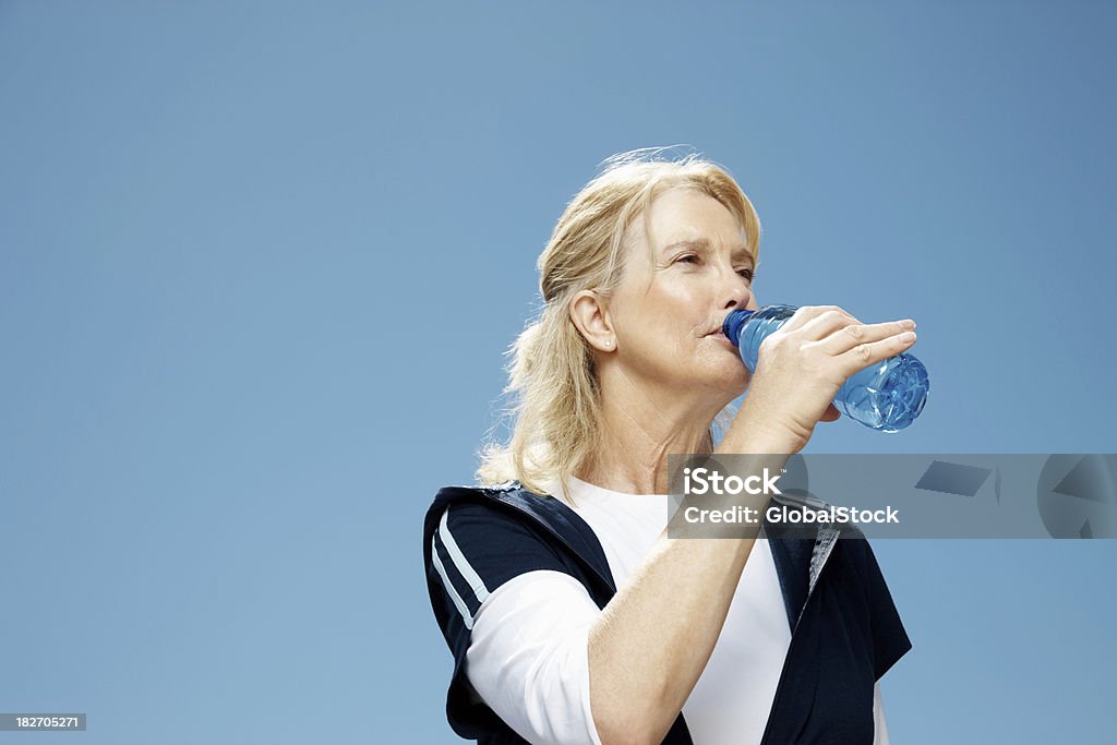 Mujer madura agua potable contra el cielo despejado - Foto de stock de 50-54 años libre de derechos
