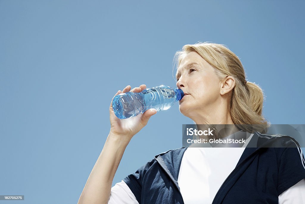 Mujer madura agua potable contra el cielo despejado - Foto de stock de 50-54 años libre de derechos