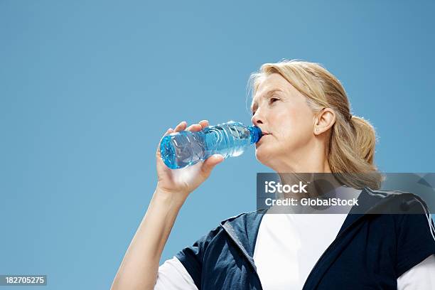 Mujer Madura Agua Potable Contra El Cielo Despejado Foto de stock y más banco de imágenes de 50-54 años