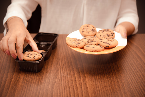 woman transfers crisp chocolate chip cookies from packaging to plate for coffee break