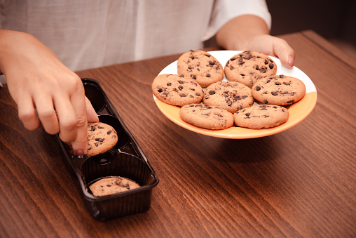 woman hand puts chocolate chip cookies from packaging on plate. close up view