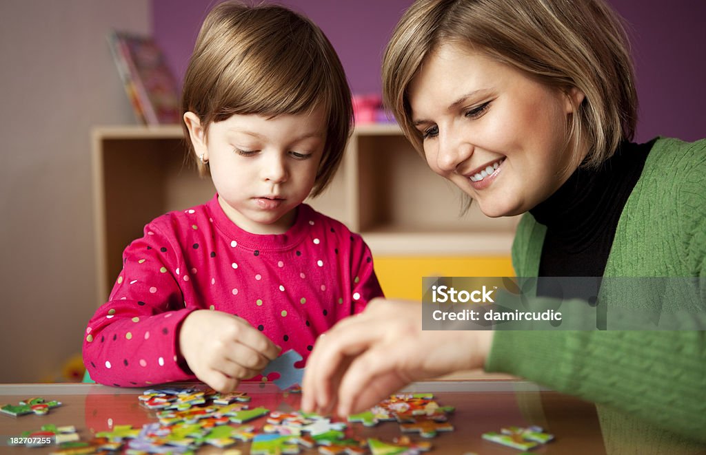 Mãe ajudando a filha com quebra-cabeça - Foto de stock de Quebra-cabeça - Jogo de lazer royalty-free