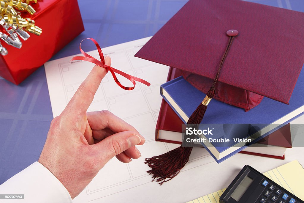 Don't Forget Finger Ribbon: Graduation, Cap, Books, Gift "This image has a hand with a red ribbon on a finger reminding you of graduation or a graduation celebration. Selective focus is on the hand and ribbon. Background elements include a blank calendar grid, a graduation gift, a graduation cap, books, a calculator, and notebook paper.Other related images:" Book Stock Photo