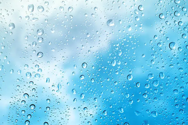 Raindrops on window with clouds.  Blue hue added.