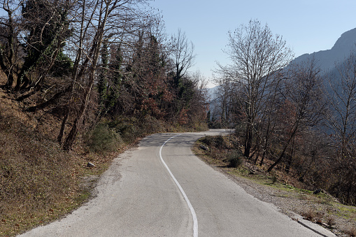 View of high, picturesque mountains, forest and a narrow highway (Greece, Epirus) on a sunny, winter day