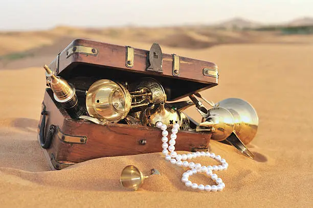 arabian origin treasures in a wooden chest lying on the desert sand. image taken in dubai