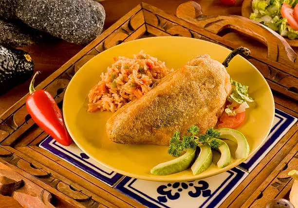 Chile Relleno or Poblano Pepper stuffed with beef and served with rice and avocado on Mexican decoration