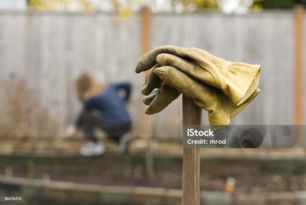 Gardening "A pair of gloves resting on a shovel, with a young woman gardening in the background, sans gloves." Adult Stock Photo
