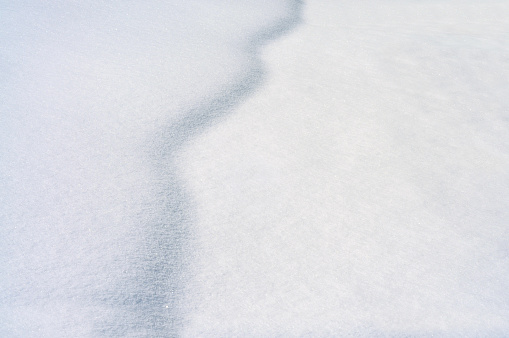 horizontal image of snow drift. the morning sun creates a shadow along the top. image has good texture.