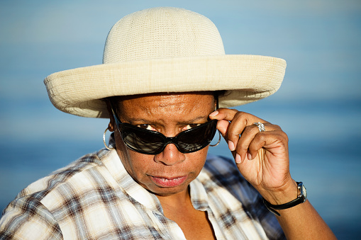 A portrait of a mature woman staring at the camera over her sunglasses.