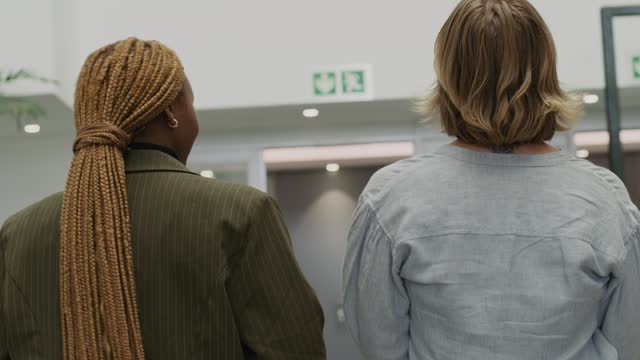 Rear view of two young multiracial woman in businesswear walking and talking in office