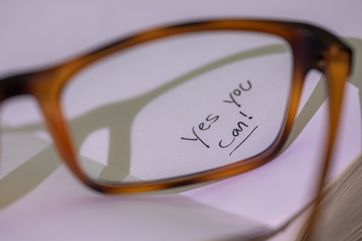 Hand written words that read Yes You Can seen thru eye glasses on a white page.