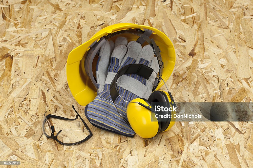 Hardhat, Work Gloves, and Ear Muffs "Protective workwear for your safety. Hard hat, work gloves, safety glasses and ear muffs on an OSB wood background.Please also see:" Chipboard Stock Photo