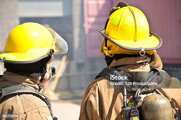 Two Firefighters Looking On At Smoking Fire Stock Photo - Download Image Now - Firefighter, Rear View, Dirty