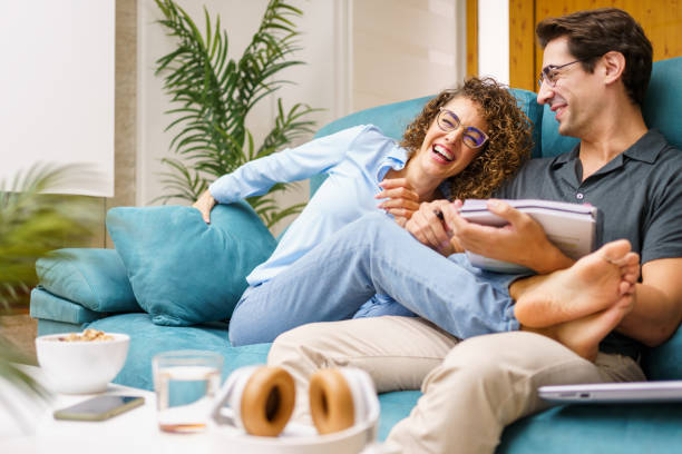 istock Happy couple with notebook sitting on sofa at home while laughing joyfully 1827234471