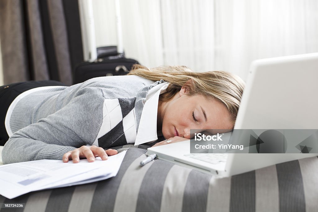 Sleeping Business Traveler Tired, Exhausted, Napping Working in Hotel Room "Subject: A young business woman tired and exhausted, fell asleep in bed in her hotel room with her laptop computer and paperwork." 20-29 Years Stock Photo