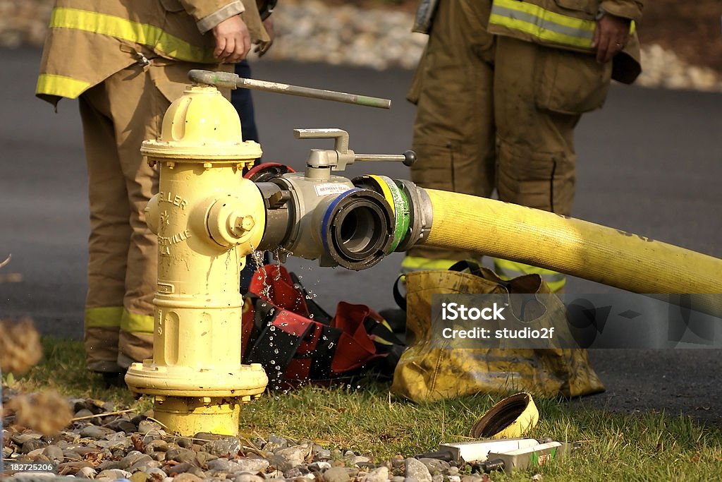 Feeding the hose Fire fighters adjust the water pressure on a yellow fire hydrant Fire Hydrant Stock Photo