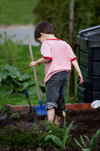 istock Young boy standing in garden bed, playfully reaches for tools 182725479