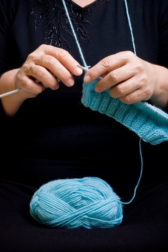 Close-up of a mature woman's hands knitting with blue yarn.