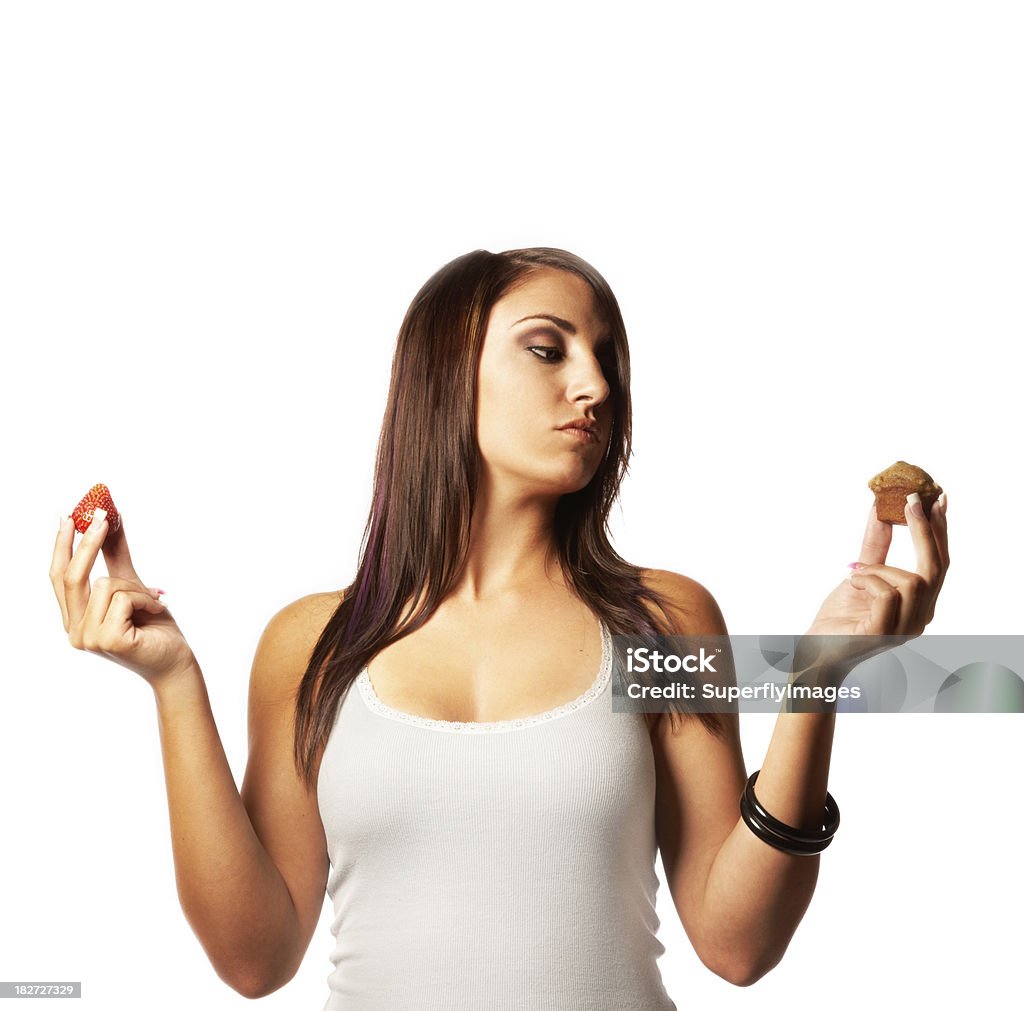 Young woman deciding which food to eat, fruit or muffin? Portrait of an attractive young woman holding a muffin in one hand and a strawberry in the other. Square shot. Isolated on white. 20-29 Years Stock Photo