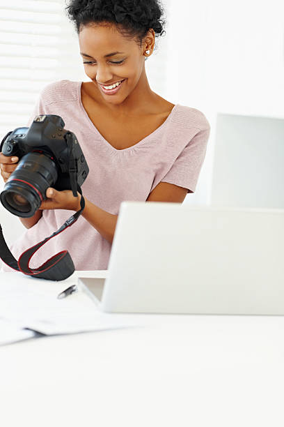 istock Young lady holding a camera with laptop on table 182727334