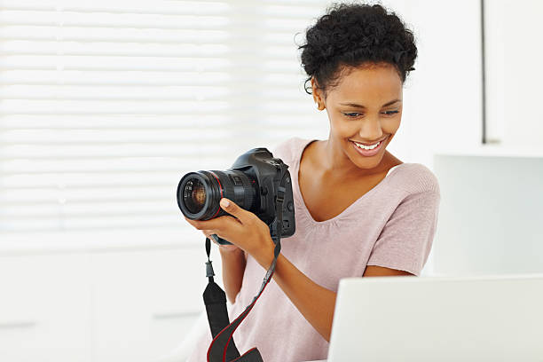 istock Young lady holding a camera while looking at laptop 182727338