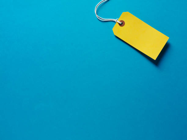 Yellow Label on a Blue Background Yellow luggage label on a blue paper background.Copy space.Click on the links below to see more of my stationary and finance images. price tag photos stock pictures, royalty-free photos & images