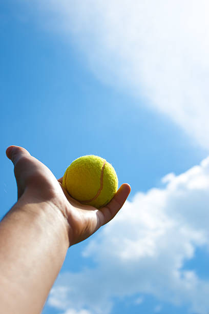 istock Tennis ball in hand against a blue sky 182730237