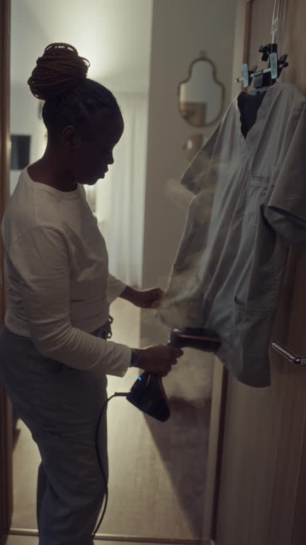 Black Female Medical Worker Steaming Uniform for Hospital Shift