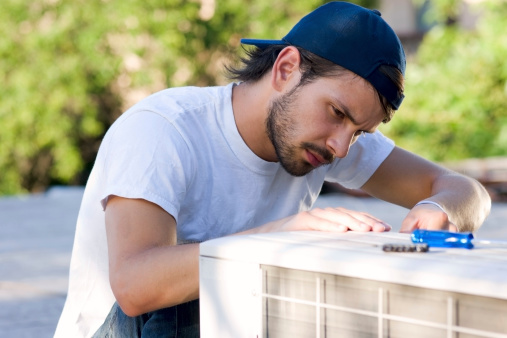 Young male serviceman with mini-split heat pump on roof top.