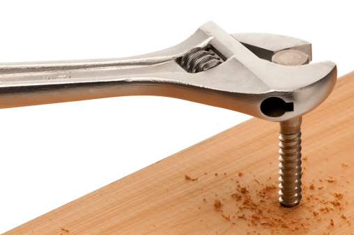 Close-up of an adjustable wrench driving a lag bolt into a board.  Isolated on white with clipping path.