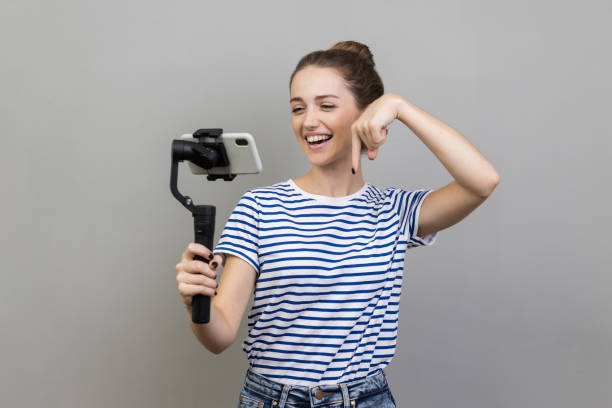 istock Woman using cell phone and steadicam for broadcasting livestream, pointing down, asking to subscribe 1827391281