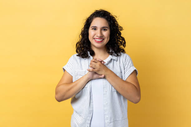 istock Woman standing looking at camera, keeps hands together, expressing happiness. 1827391653