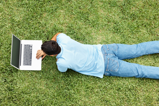 Top view of a casual young man using laptop while lying on grass