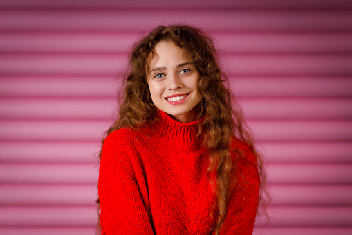 Happy smiling young adult woman wearing winter red sweater indoors looking at camera with joyful smile